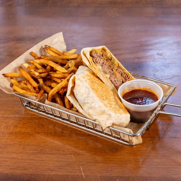 A metal basket holds golden french fries, a sliced burrito with meat and cheese, and a side of dipping sauce.