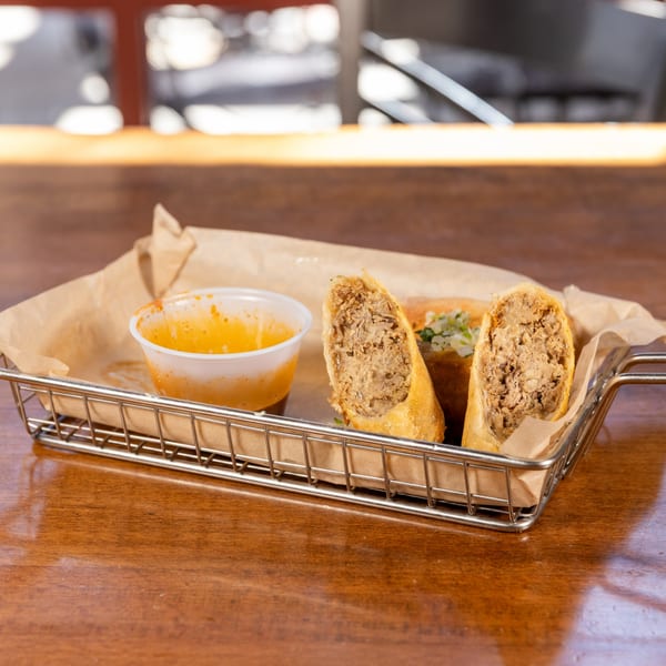 Crispy egg rolls filled with savory meat, served in a metal basket with a side of dipping sauce.