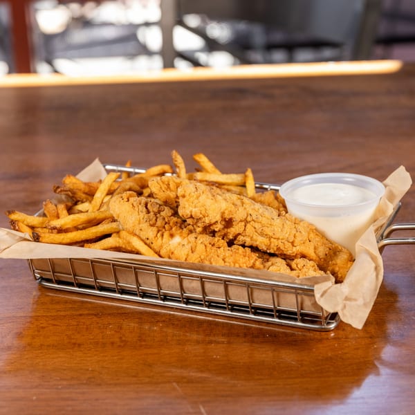 A metal basket of crispy chicken tenders and golden french fries with a side of dipping sauce.