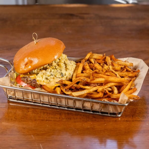 A juicy cheeseburger with relish and golden fries served in a metal basket on a wooden table.