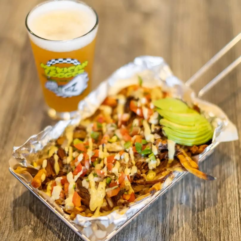 Loaded fries topped with avocado, pico de gallo, and sauce, served with a glass of beer.