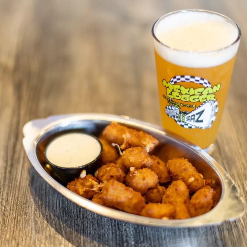 Fried cheese curds with dipping sauce in a metal dish next to a glass of Mexican Logger beer.