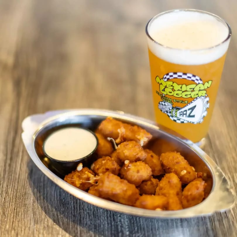 Fried cheese curds with dipping sauce and a glass of Mexican Logger beer on a wooden table.