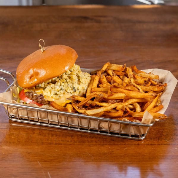 A Brews burger with cheese, lettuce, tomato, and relish, served with golden fries in a metal basket.